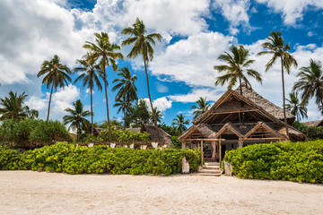 View of the house with thatched roof located among the palm trees on Matemwe Beach, Zanzibar, Tanzania, Africa - obrazy, fototapety, plakaty
