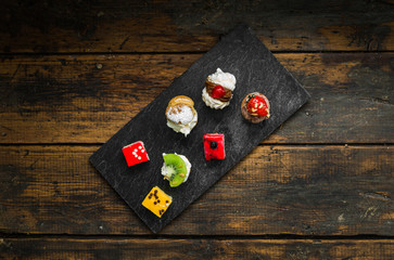 Selection of different dessert pastry sweet mini cakes and tartlets with cream and fruit on slate and wooden background