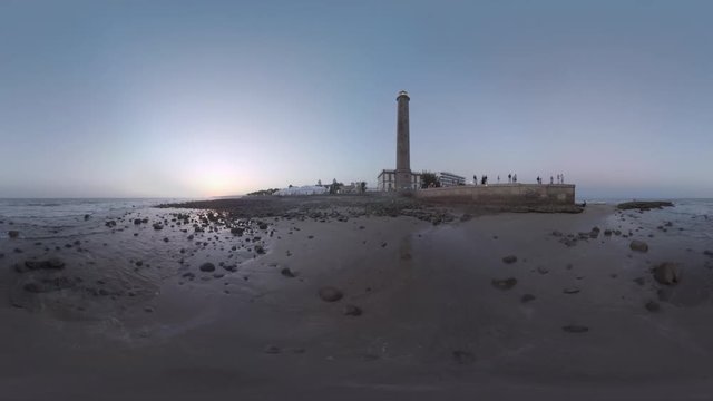 360 VR Video. Evening scene with quiet ocean, resort and people with faces unidentified walking at the bottom of Maspalomas Lighthouse. Gran Canaria, Spain