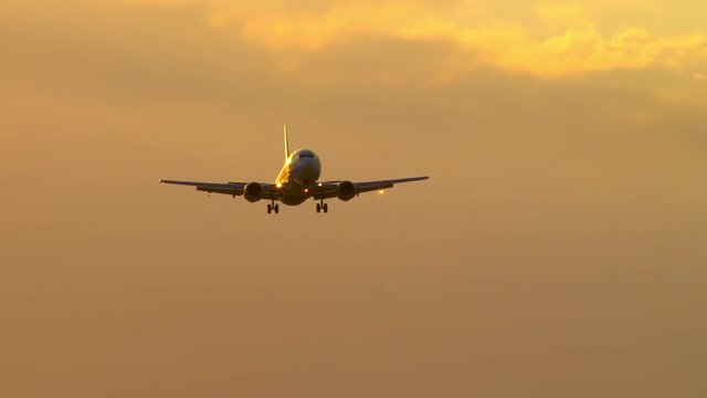 Generic Boeing 737 Commercial Passenger Jet Airliner Flying in a Vibrant Orange Sunlight Sky with a Cloudy Background