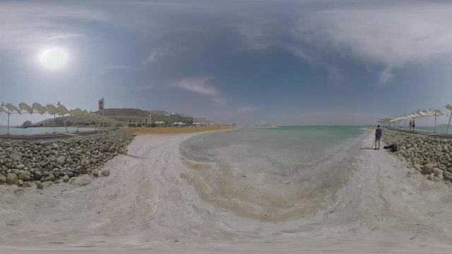 360 VR video. Dead Sea landscape with resort on its shore. Tourists walking on the rock fill path and taking photos of nature landmark. Earth lowest elevation on land