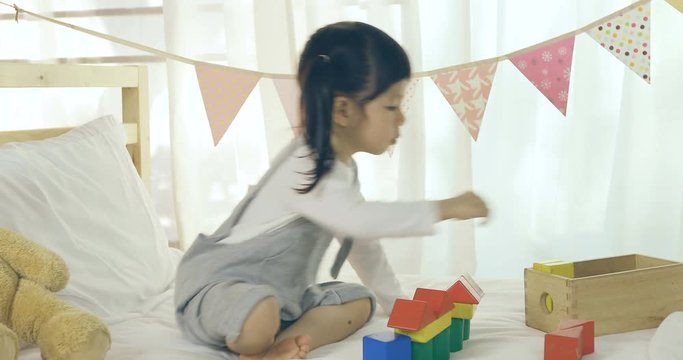 Child little girl playing with colorful wooden blocks on the bed in the bedroom, Comfortable children at home concept