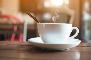 White cup with steaming hot coffee on table with bokeh background at cafe