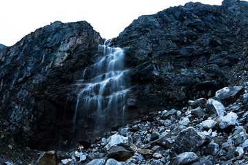 Large mountain waterfall in the mountains on the dark wet rocks, evening landscape long exposure