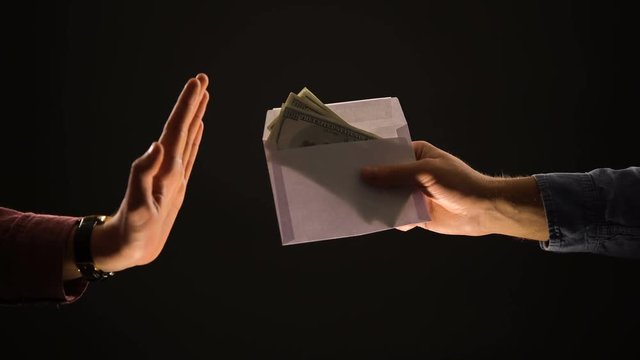 Male giving envelope with dollars, person making stop gesture, refusing bribe
