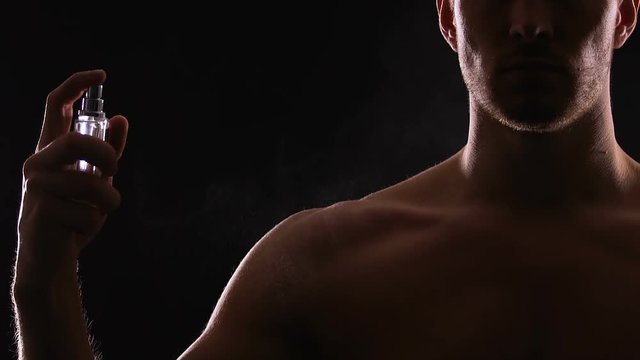 Athletic man spraying perfumes on torso, seductive fragrance for dating, slow-mo
