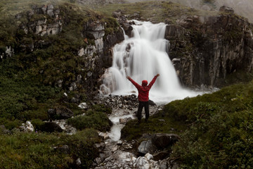 man stands under a mountain waterfall in the misty valley of Iceland