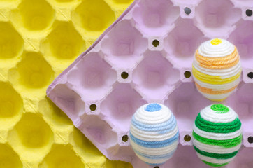 Colorful eggs decorate with knitting wool for Easter day and festival put in purple and yellow egg tray that have space for text.
