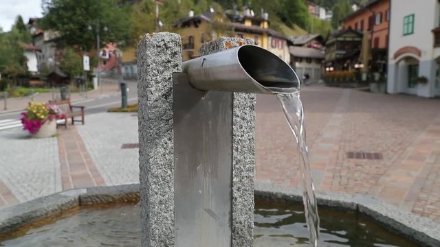 Water is coming out of tube of smal fountain at the central square of Moena city in Italian Dolomites filmed in slow motion.