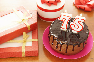 Birthday celebration at seventy five years. A cake with burning candles in the form of numbers and a lot of gifts on a table