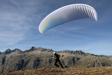 Paraglider Pilot takes off with his paraglider to take off and fly into the valley in the Swiss Alps