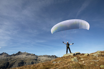 Paraglider pilot stands on a rock and balances his paraglider above his head near Lake Grimsel in the Swiss Alps