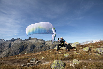 Paraglider pilot sits on a rock and balances his paraglider above his head near Lake Grimsel in the...
