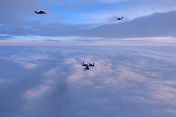 Skydivers are falling above pink sunset clouds.