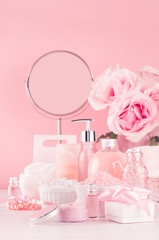 Modern youth bathroom or dressing table design in pastel pink color - fresh pink flowers, cosmetic products, bath accessories, jewelry, round mirror on white wood board.