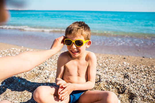 A boy in sunglasses plays on the beach.