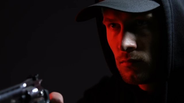 Man in hoodie pointing gun, armed robbery at night or contract killing, closeup
