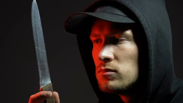 Sinister man looking at knife isolated on black, maniac preparing to kill