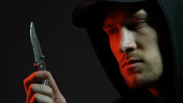 Hooded man viewing folding knife, preparing for armed robbery, pickpocketing