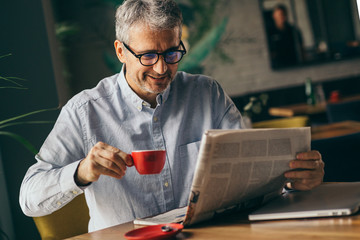 morning routine. man reading newspaper in cafeteria and drinking coffee