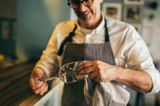 Middle aged barman polishing the wine glass in cafe bar