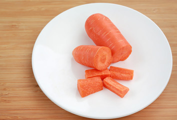 Chopped carrot on white plate against wooden board. 