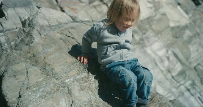 Little toddler sliding down rock on the beach