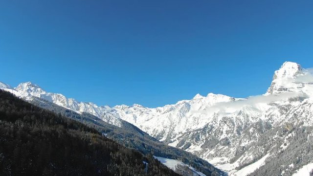 Aerial view and reveal of snowy mountain winter snow on a sunny day, blue sky and sun, perfect for ski resort