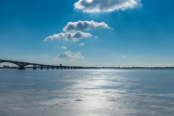 Beautiful winter landscape with a bridge over a frozen river and clouds in the blue sky