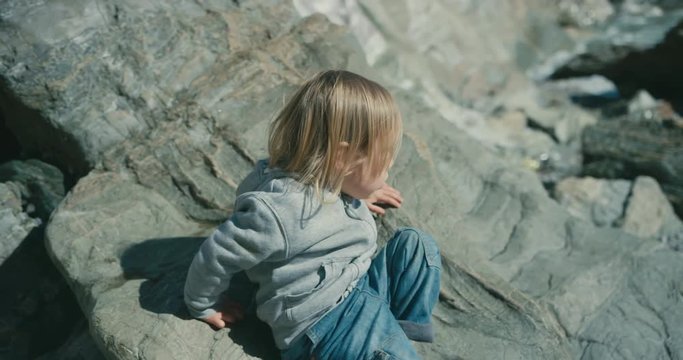 Little toddler sitting on a rocky beach