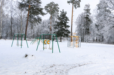 playground with swings, benches, slide and sports units in  snow.