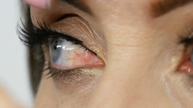Beautiful middle-aged adult model with blue eyes applying eyeliner closeup. Professional make-up artist applying black eyeliner. Long false eyelashes