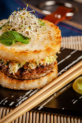 Pan-Asian cuisine concept. Japanese sushi burger made from rice bread, chicken and pork meat patties, lettuce and wasabi sauce. Serving dishes with french fries. copy space