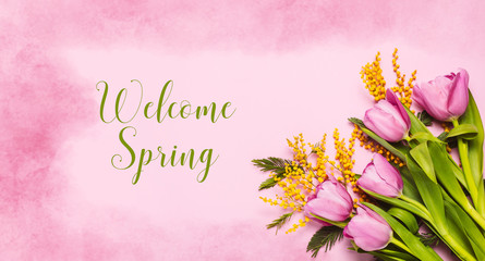Obraz premium Pink tulips and mimosa flowers on pink watercolor background. Spring greetings. Text Welcome Spring. Flat lay, top view