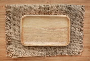Square wooden tray on sack against wood board background. Top view.