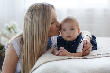 Young mother holding her newborn child.Woman and new born boy relax in a white bedroom.A young mother gently holds her newborn son in her arms.Family at home.Young mother playing whith her newborn son