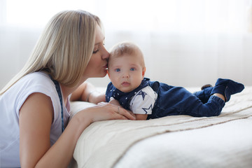 Young mother holding her newborn child.Woman and new born boy relax in a white bedroom.A young...