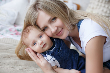 Young mother holding her newborn child.Woman and new born boy relax in a white bedroom.A young mother gently holds her newborn son in her arms.Family at home.Young mother playing whith her newborn son