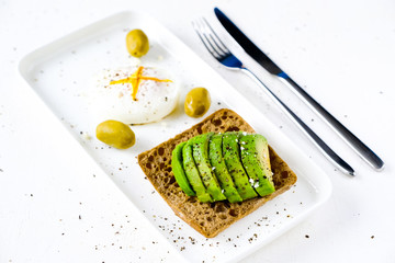 Healthy food concept: toast with avocado, green olives and poached egg