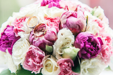 wedding rings on bouquet of white, purple and pink peonies