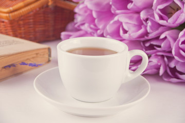 A cup of tea, book and violet tulips on the table