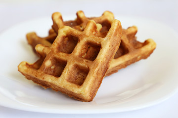 Belgian waffles in white plate. Healthy breakfast close up, pieces of freshly baked classic wafer