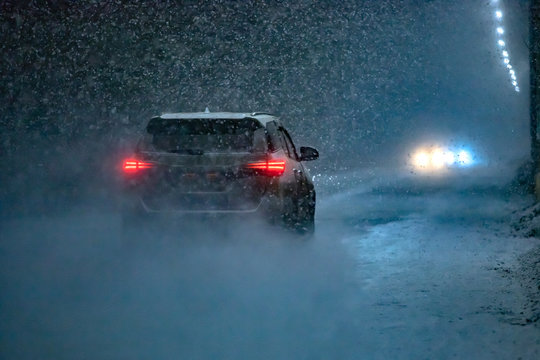 The car goes on the road in an unexpected spring snowfall in the evening.