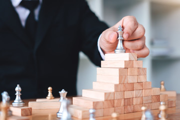 Businessman hand picking chess on top block wood about leadership concept.