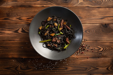 black noodle with marbled beef in a black plate on a wooden background