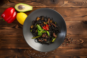 black noodle with marbled beef in a black plate on a wooden background