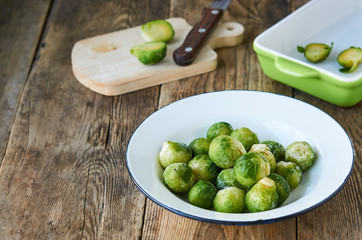 Frozen brussels sprouts in a white bowl on a wooden background