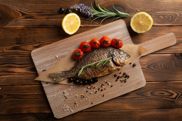 Japanese-style dorado with tomatoes, olives and spices on a wooden background