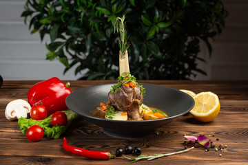 baked lamb shank with oriental herbs with vegetables on wooden background