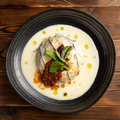 warm eggplant with spinach and parmesan milk in a black plate on a wooden background
